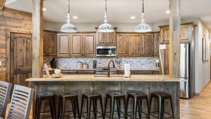 Uma cozinha com armários de madeira, uma ilha central com banquetas, eletrodomésticos de aço inoxidável e iluminação pendente.