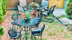 A patio with a round table and chairs, surrounded by a brick wall and a wooden fence. - Walk to ACRISURE in 23 Mins!  King Bed + FREE private park ✭Perfect Locale✭ (Pittsburgh)