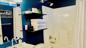 A bathroom with a sink, toilet, and bathtub. There are shelves with toiletries and towels. - Walk to ACRISURE in 23 Mins!  King Bed + FREE private park ✭Perfect Locale✭ (Pittsburgh)