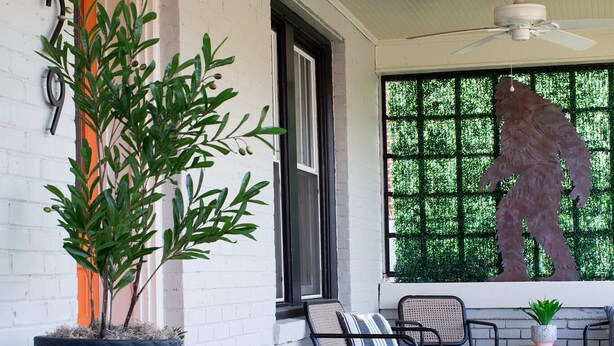 A covered porch with a large potted plant, outdoor seating, and a decorative lantern.