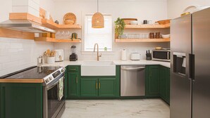 A modern kitchen with green cabinets, a stainless steel refrigerator, a built-in oven, and a double sink.