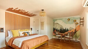 A bedroom with a wooden bed, a mural on the wall, and a dining area with chairs.