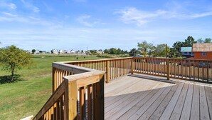 A wooden deck with a railing overlooking a grassy area and houses in the distance. - Fishermen's Catch (Frederica)