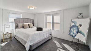 A bedroom with a bed, bedside table, lamp, and a painting of a sea turtle. - Fishermen's Catch (Frederica)