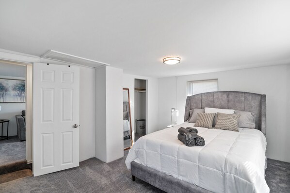 A bedroom with a large bed, a wardrobe, a mirror, and a door leading to another room. - Fishermen's Catch (Frederica)