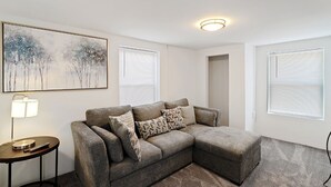 A modern living room with a sectional sofa, a lamp, and a painting on the wall. - Fishermen's Catch (Frederica)