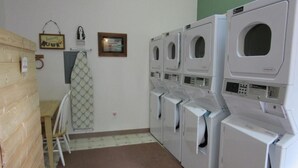 A laundry room with multiple washing machines and dryers, wooden walls, a small table, and a towel rack. - Box Canyon "Moose Cabin"-4 bed, private bath, WIFI (Seward)