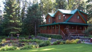 A log cabin with a porch, surrounded by a well-maintained garden and dense forest. - Box Canyon "Moose Cabin"-4 bed, private bath, WIFI (Seward)