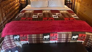 Una camera in baita di legno con un letto, due lampade da comodino, una coperta rossa e una panca.