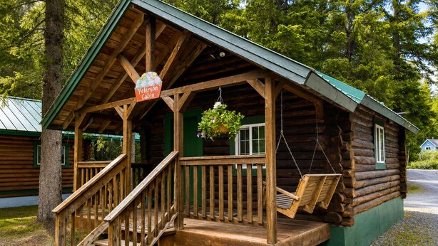 Una baita con veranda, scale in legno e un cesto di fiori appeso.