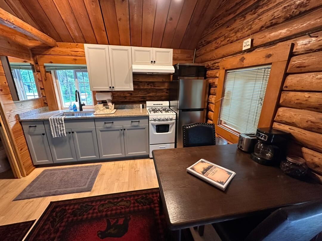 A compact kitchen with wooden walls, a stove, refrigerator, and a dining table with a placemat.
