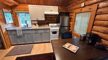 A compact kitchen with wooden walls, a stove, refrigerator, and a dining table with a placemat.