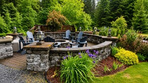 A stone fire pit with seating, surrounded by a stone wall and garden. - Box Canyon Cabin Bear's Den Cabin - 2 bed, WI-FI (Seward)