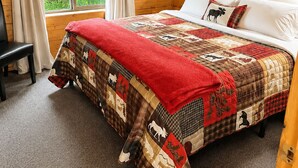 A wooden cabin bedroom with a large bed, a bench, and a window with curtains. - Box Canyon Cabin Bear's Den Cabin - 2 bed, WI-FI (Seward)