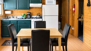 A wooden interior with a dining table, chairs, cabinets, a microwave, a refrigerator, a kettle, and a fire extinguisher. - Box Canyon Cabin Bear's Den Cabin - 2 bed, WI-FI (Seward)