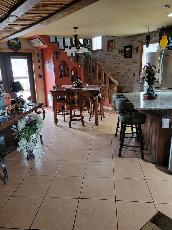 A dining area with a wooden table and chairs, a kitchen counter with a vase of flowers, and a staircase leading to another level.