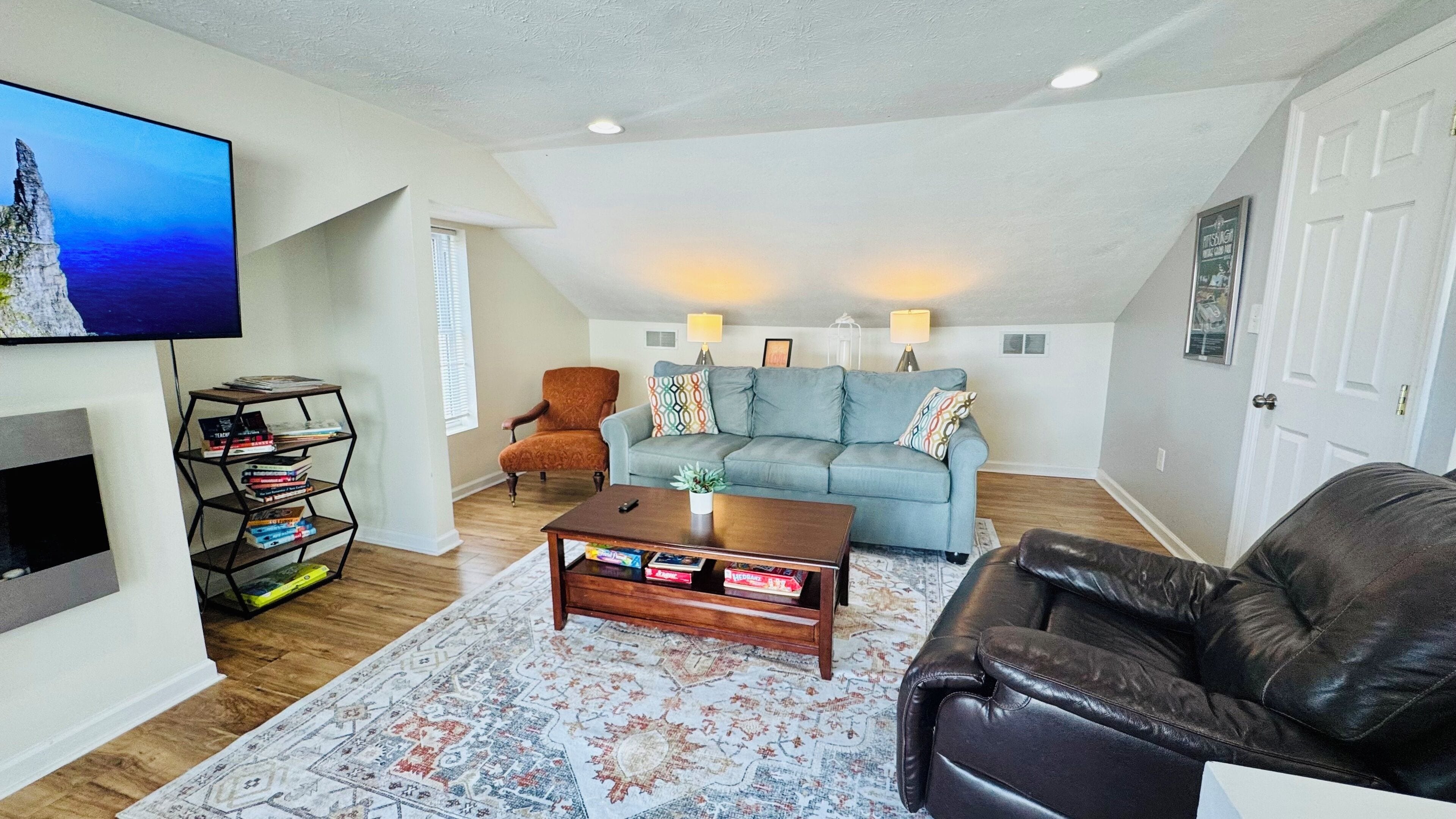 A spacious living room with a high ceiling, a large TV, a sofa, a coffee table, and a leather chair.