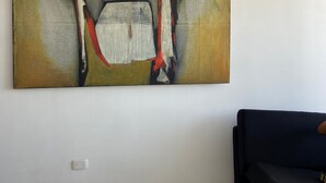 A large abstract painting on a plain wall in a room with a dark-colored sofa and a tiled floor. - 3TP-27 APARTAMENTO DE 3 HABITACIONES (Cartagena)