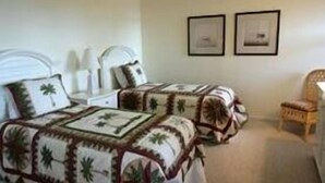 A room with two beds, each with a patterned bedspread, a chair, and two framed pictures on the wall.