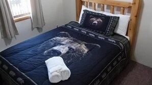 Een slaapkamer met een houten hoofdbord, een bed met een donkerblauwe dekbedovertrek met dierenprint, een wit kussen en een kussen met een beer thema.