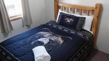 Een slaapkamer met een houten hoofdbord, een bed met een donkerblauwe dekbedovertrek met dierenprint, een wit kussen en een kussen met een beer thema.
