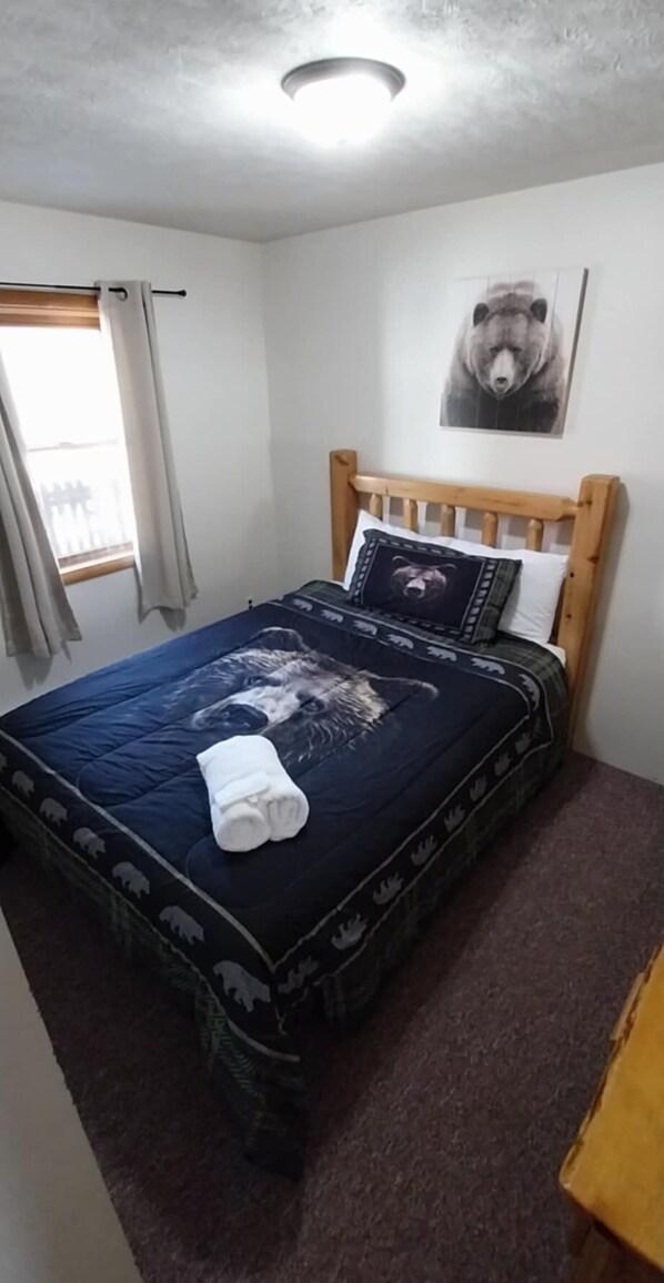 A bedroom with a wooden headboard, a bed with a dark blue bedspread featuring animal prints, a white pillow, and a bear-themed pillow. - Family suite in Ohiopyle-Walk to Falls & Trals (Ohiopyle)