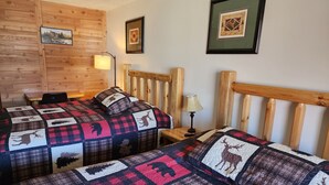 Une chambre chaleureuse avec deux lits, des têtes de lit en bois et une couvre-lit matelassé orné de motifs animaliers.