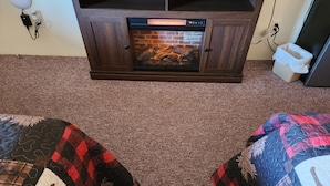 A room with a fireplace, carpeted floor, and two beds with patterned bedding.