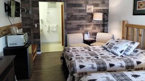 Un dormitorio con cama, dos sillas, una mesita de noche, una lámpara, microondas y un panel de pared de madera.