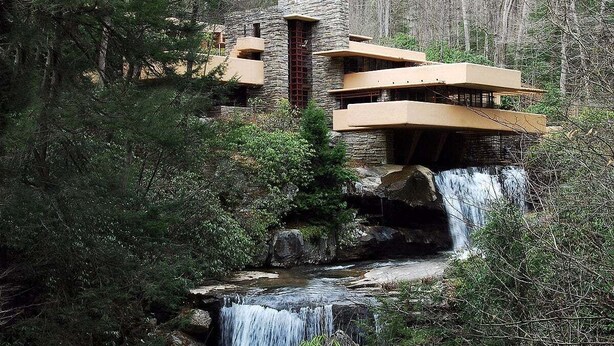 Un edificio moderno con múltiples balcones que dan a una cascada en zona boscosa.