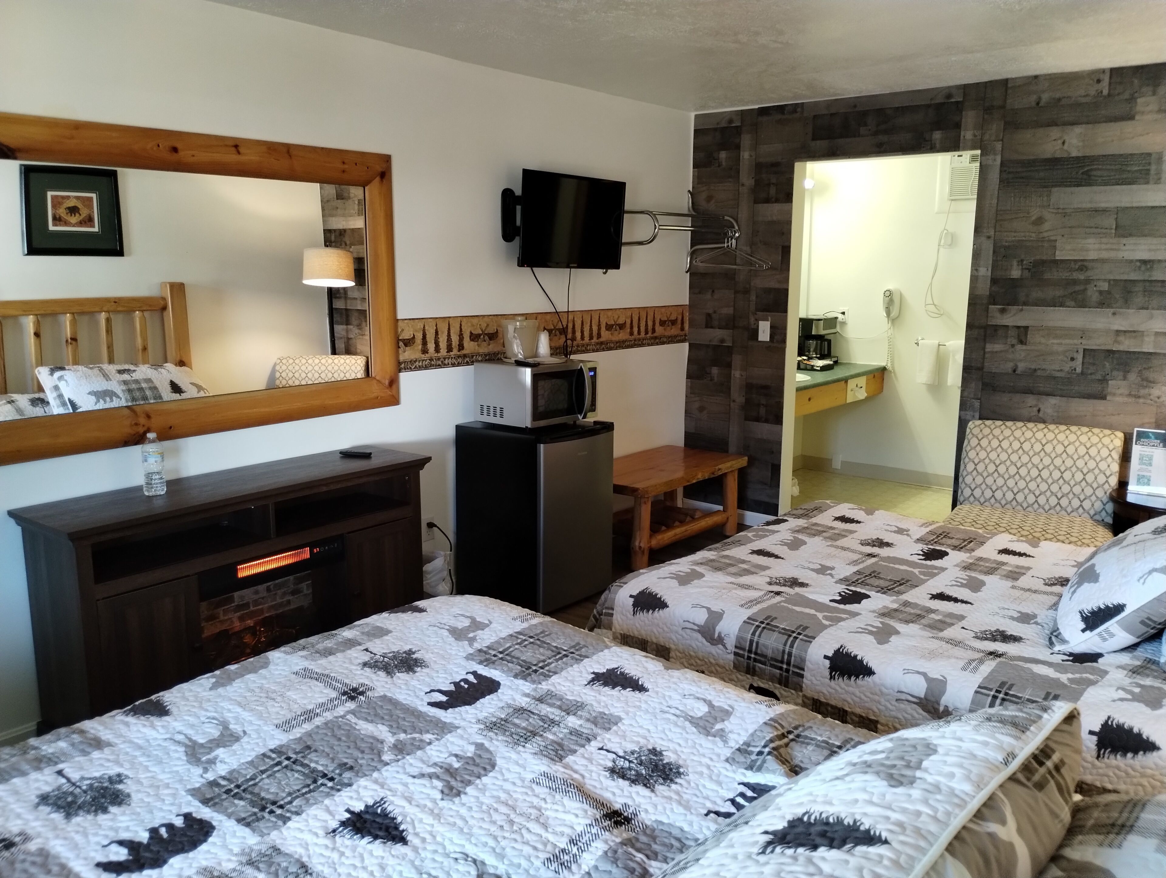 Habitación de hotel con dos camas, televisión, microondas, escritorio pequeño y baño visible a través de una puerta abierta.