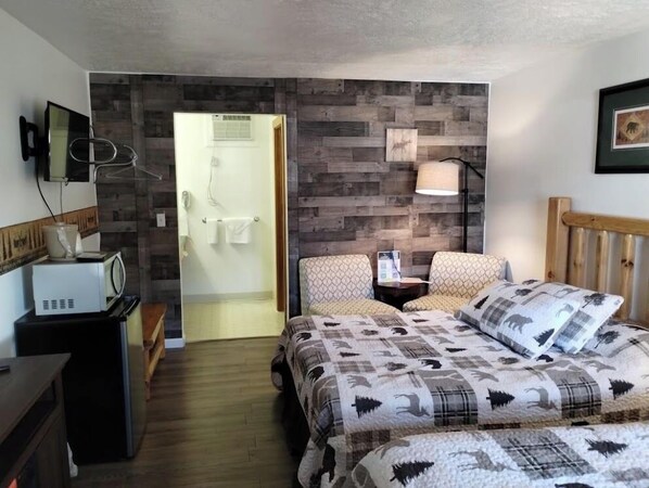 A bedroom with a bed, two chairs, a bedside table, a lamp, a microwave, and a wooden wall panel.