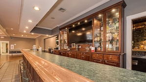 A bar area with a long wooden counter, a large wooden cabinet with glass doors displaying bottles, and a television above the counter.