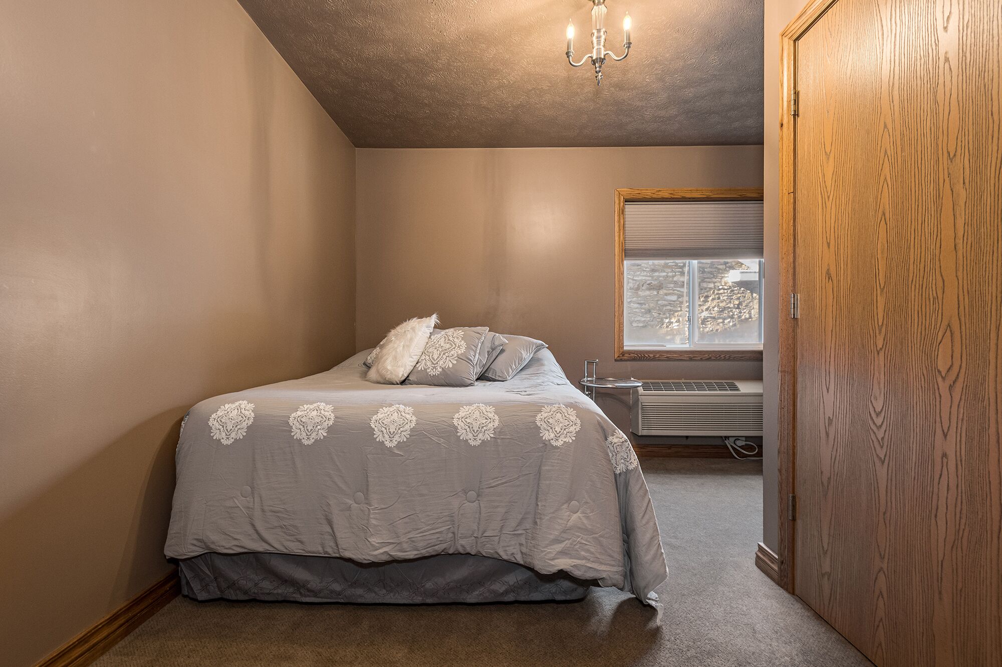 A bedroom with a bed, a window, a radiator, and a wooden door.