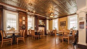 A dining area with wooden tables and chairs, a decorative ceiling, and a vintage ballot box. - JV Thompson | Jacuzzi Tub Historic Inn Room (Farmington)
