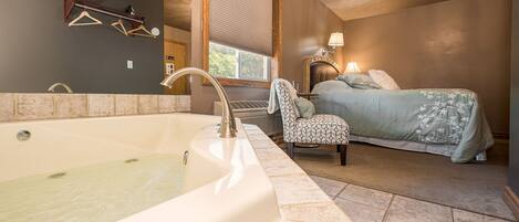 Une chambre avec une grande baignoire, un lit avec une literie à motifs floraux, un fauteuil et un lustre.