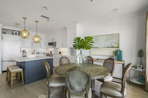 A modern kitchen with white cabinets, a central island, and a dining area with a round table and chairs.