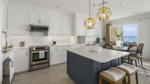 A modern kitchen with white cabinetry, stainless steel appliances, and a large island with bar stools. - SPECTACULAR CONDO, GULF-FRONT, VIEWS, POOL, GRILL, LG. PATIO, PRIVATE BEACH (Santa Rosa Beach)