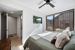 A bedroom with a bed, a ceiling fan, a window, and a view of a wooden building outside.