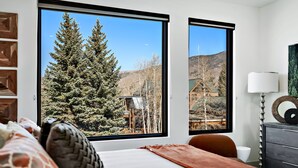 Une chambre dotée d’une grande fenêtre donnant sur une forêt et des montagnes.