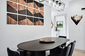 A modern dining area with a dark oval table, black chairs, and a geometric wood and black wall art.