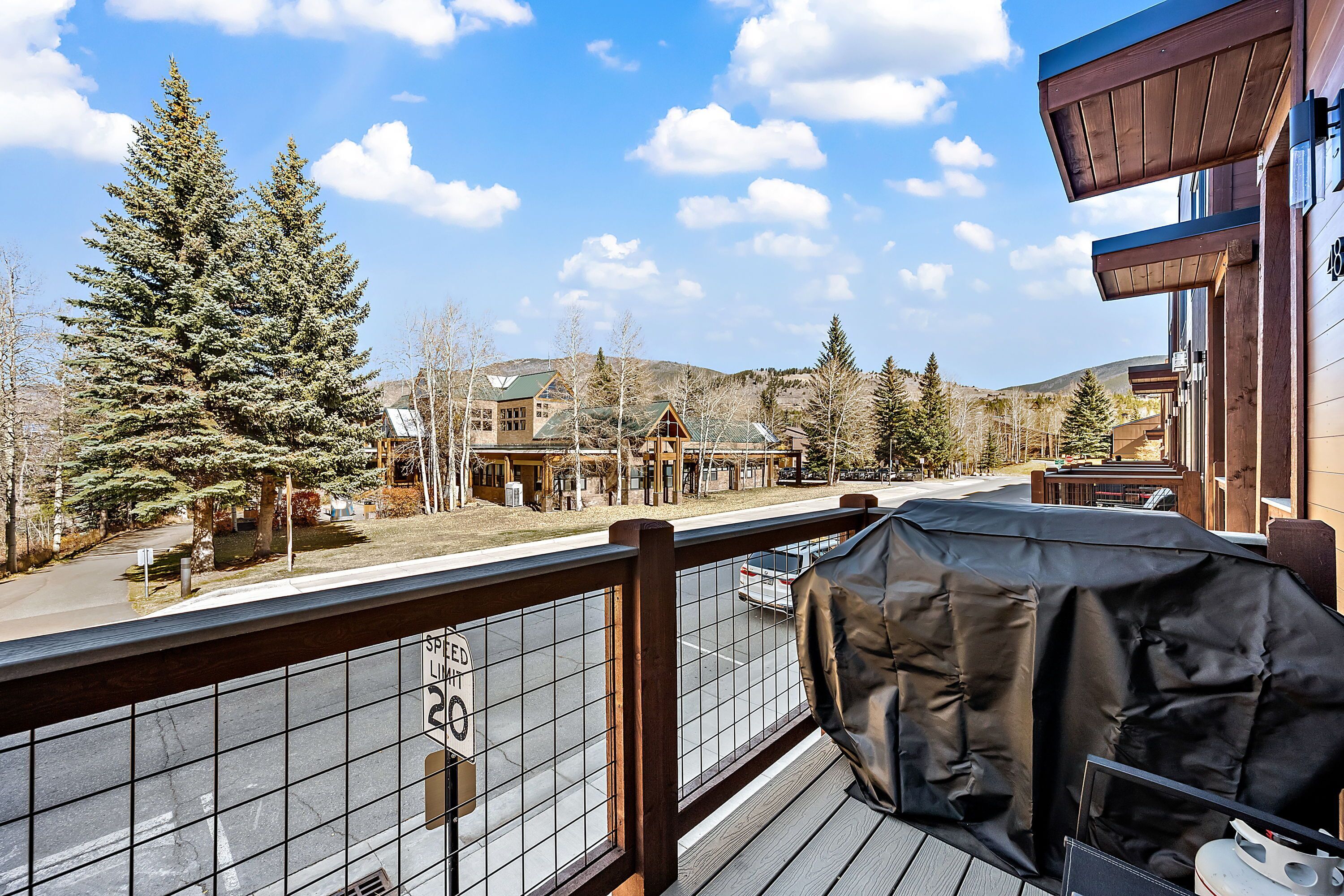 A balcony with a view of a street, a covered grill, and a sign indicating a speed limit of 20 mph.