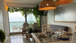 Un coin repas avec une table en verre, des chaises blanches et une vue sur l’océan.