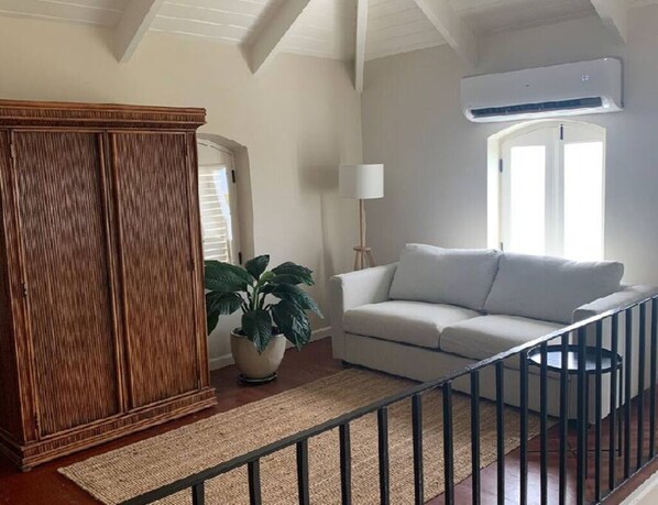 Una sala de estar con un sofá blanco, una planta grande en maceta, un mueble de madera y un ventilador de techo.