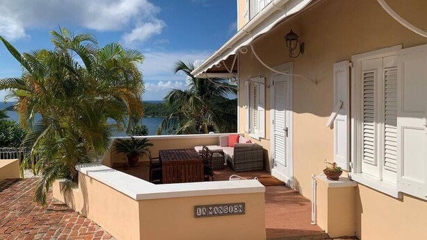 En balkon med udsigt over havet, palmer og et skilt med teksten "LA MANSION".