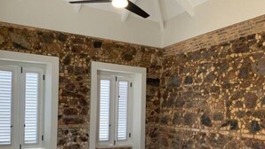 Un dormitorio con pared de piedra, cama de madera y ventilador de techo.