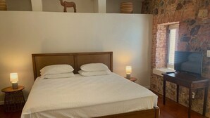 En pænt redt seng i et rum med stenvægge, et fjernsyn på et træbord og en lille lampe på et natbord.