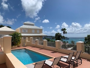 A pool area with lounge chairs, a view of the ocean, and a building with a white roof. - La Terazza w/ Queen Bed (Charlotte Amalie)