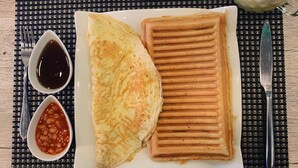 A plate with a crepe and a waffle, accompanied by two small bowls of sauces and a jar of pickled vegetables on a woven placemat. - THE GRID RESIDENCE (Lagos)