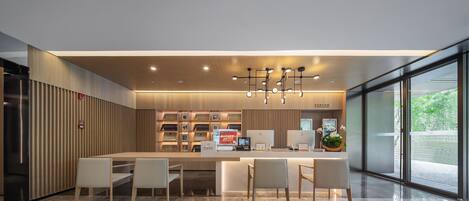 A modern reception area with a central desk, seating, and a large window offering a view of greenery.